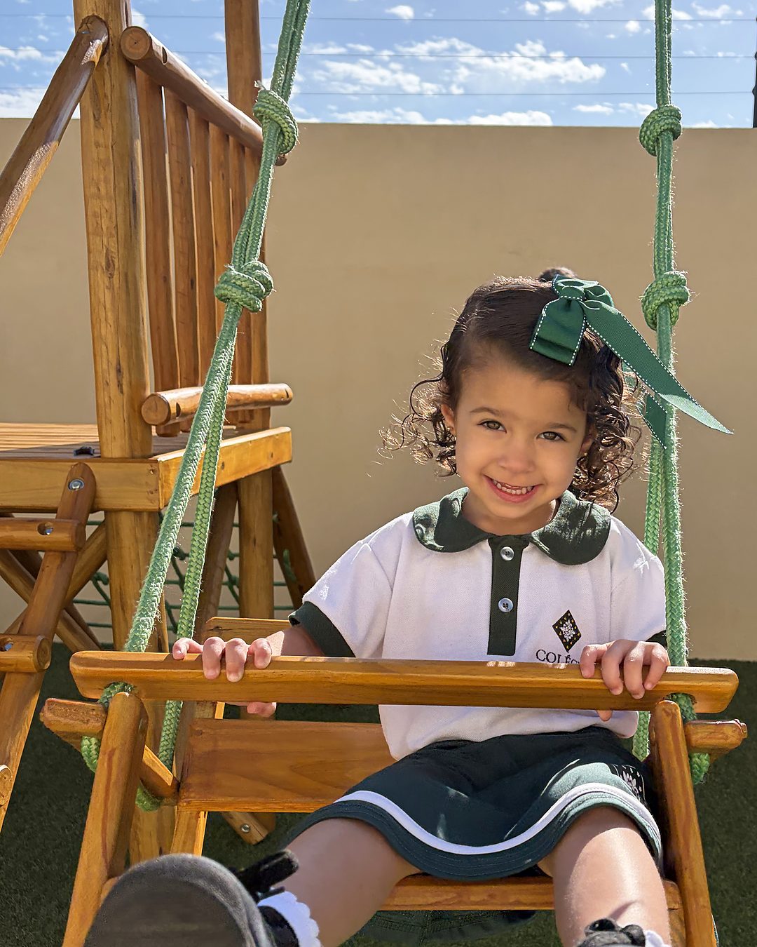 Aluna do Colégio Lírios de uniforme, sorrindo no balanço do parque